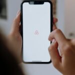 Close-up of hands holding a smartphone with Airbnb app logo on the screen indoors, highlighting modern technology.